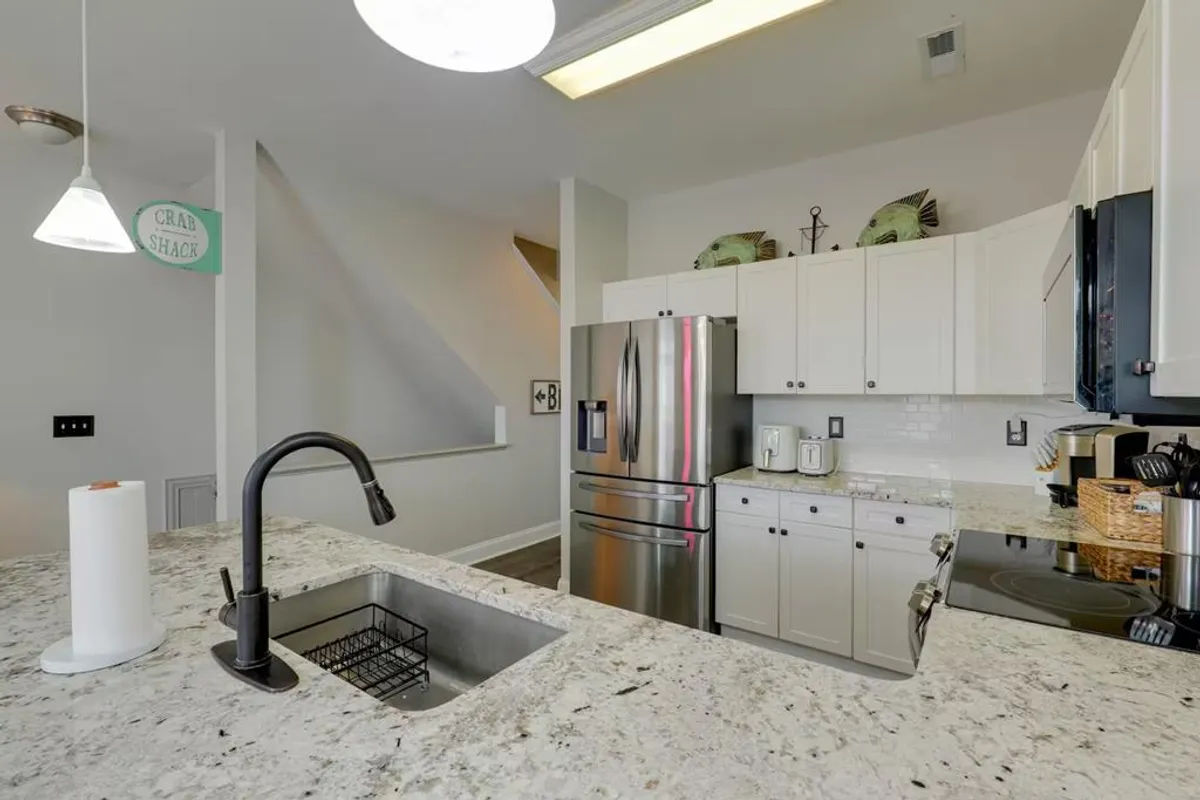 A welcoming kitchen with granite countertops, stainless steel appliances, and a large island with bar seating. Decorative fish accents bring a coastal touch to the space, while the setup encourages guests to gather around during meal prep or casual dining.