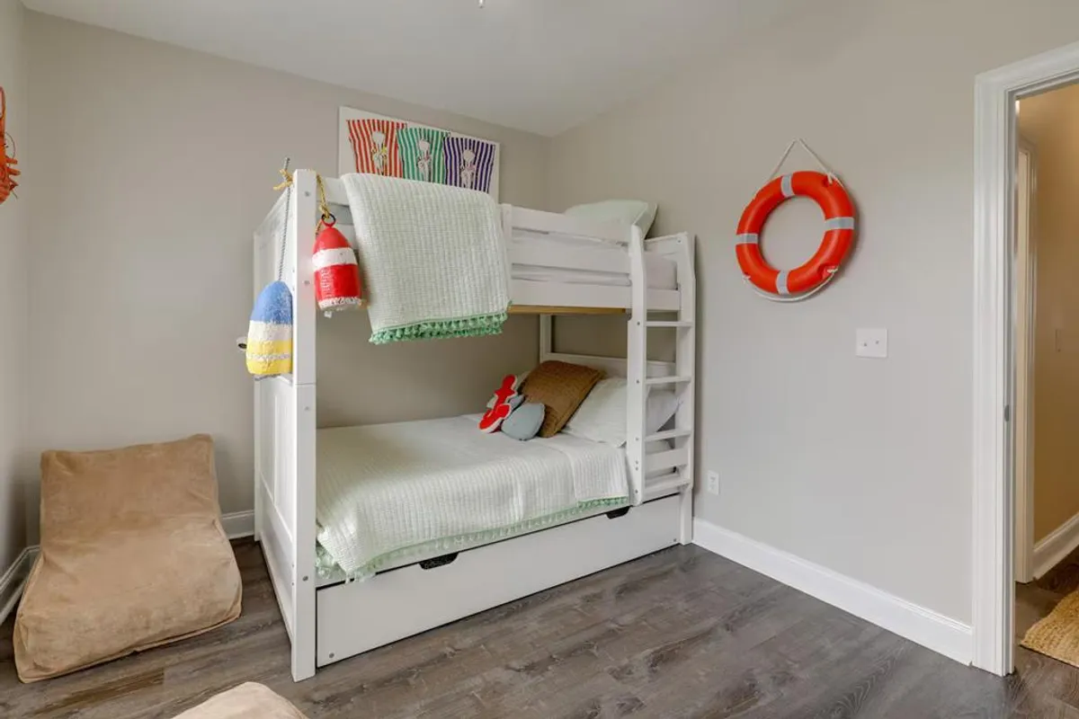 A vibrant bunk room with a full-over-full bunk bed, a bean bag chair, colorful artwork, and a decorative life preserver. The space looks playful and spacious, perfect for kids or families.