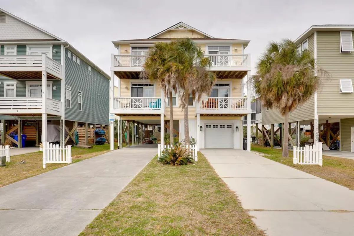A welcoming exterior shot of the three-story house, palm trees, and a driveway leading to an easy-entry garage. The scene is inviting, with plenty of space for arrivals and outdoor activities.