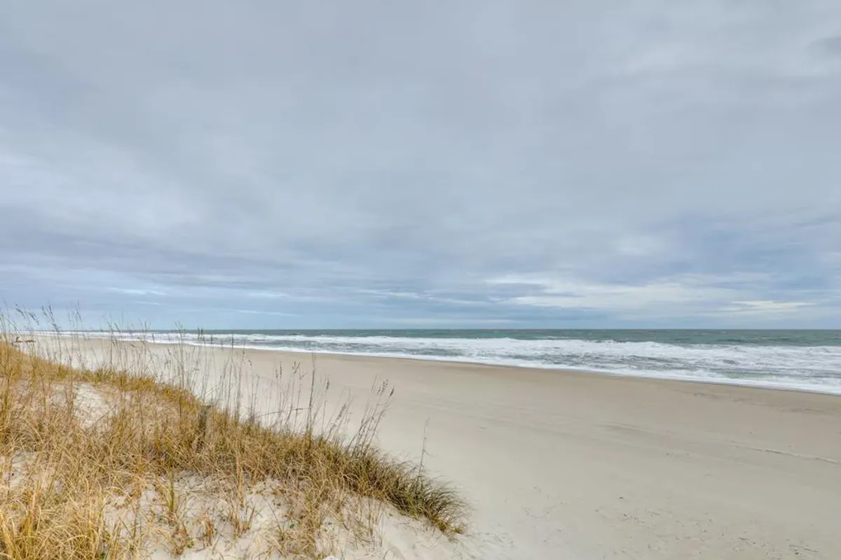 A broad view of the sandy beach with rolling ocean waves, bordered by dune grass. People can be seen beachcombing and walking along the shore, enjoying the laid-back yet adventurous beach environment. The image captures the natural beauty and active possibilities of the local coastline.