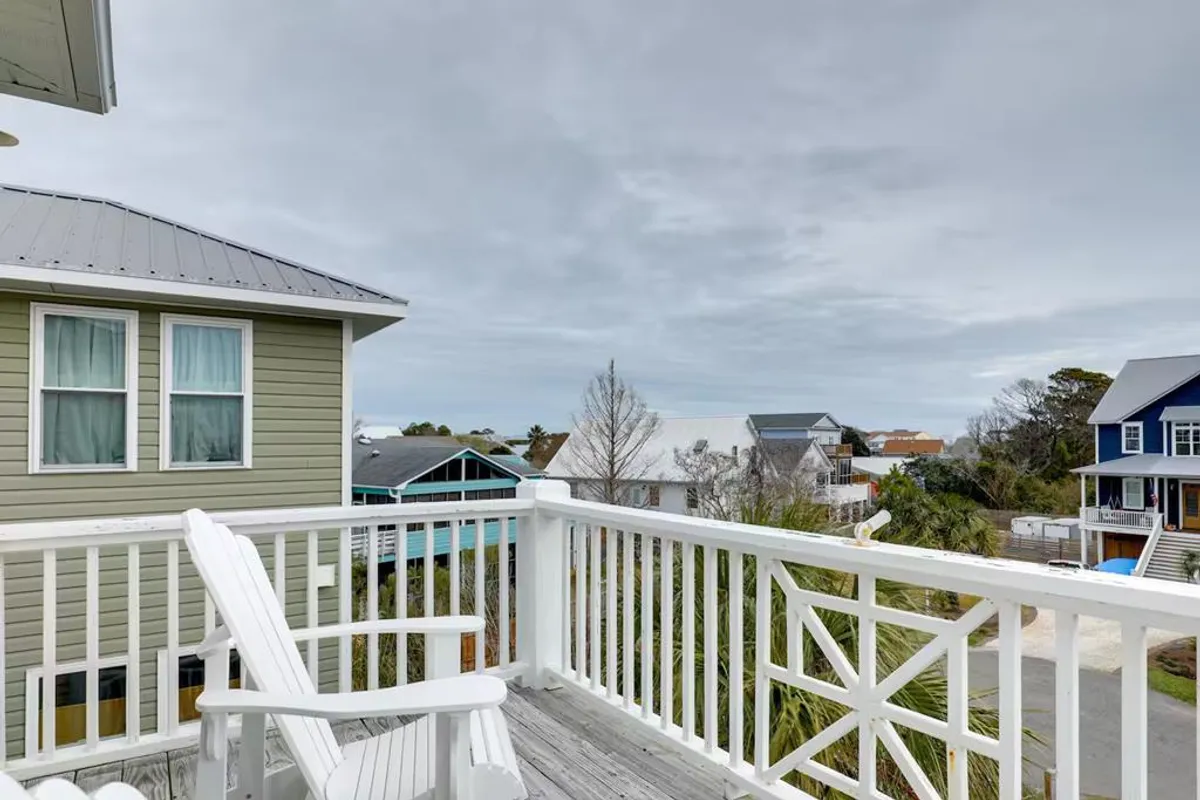 This image features a tranquil adirondack chair set on a porch or deck, overlooking neighboring houses. The scene is open to the outdoors and suggests a peaceful, leisurely moment, with ample space for relaxing and enjoying fresh air.