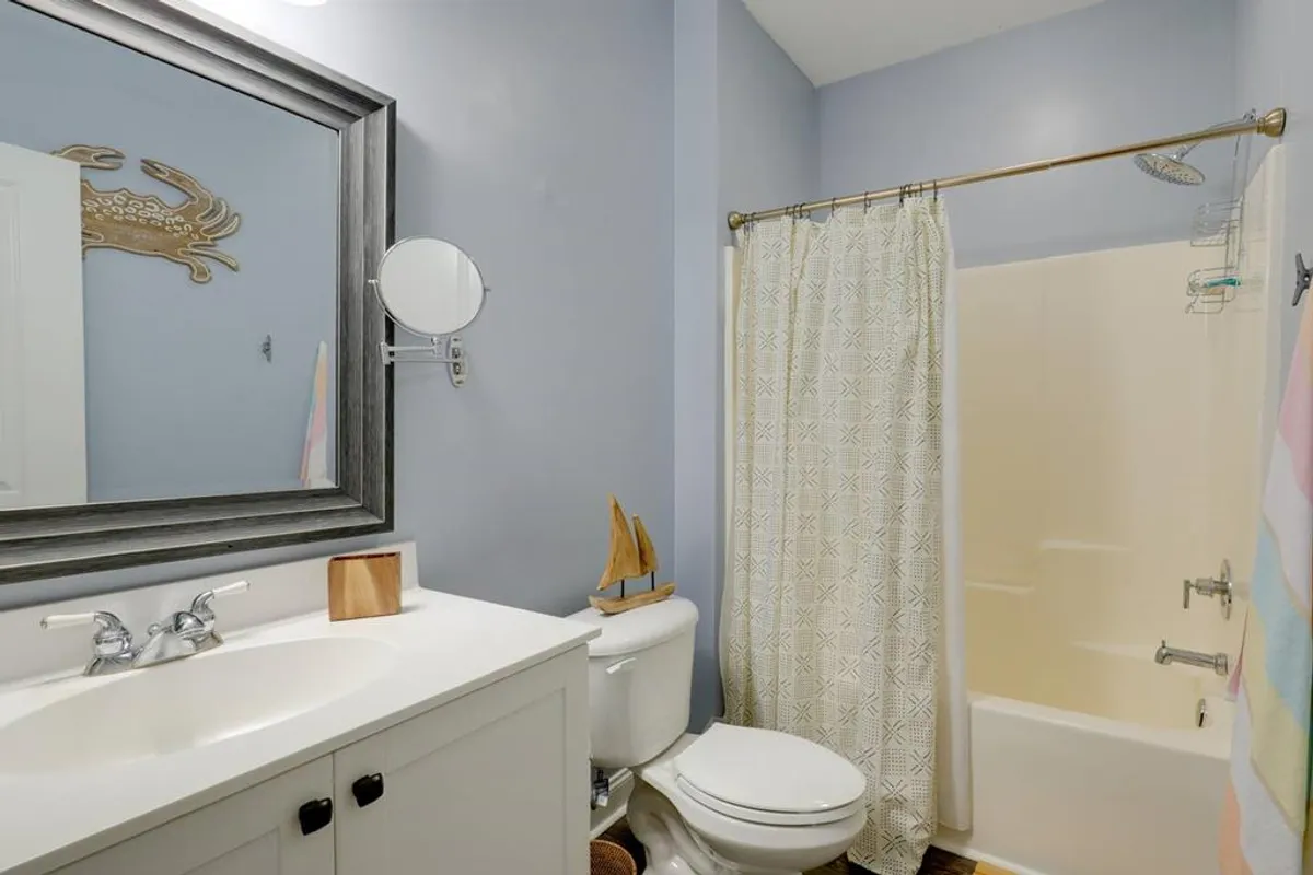 A calming bathroom with a framed mirror, decorative crab wall art, sailing ship decor, and a textured shower curtain. The space feels tranquil and well-appointed, suitable for moments of relaxation or morning routines.