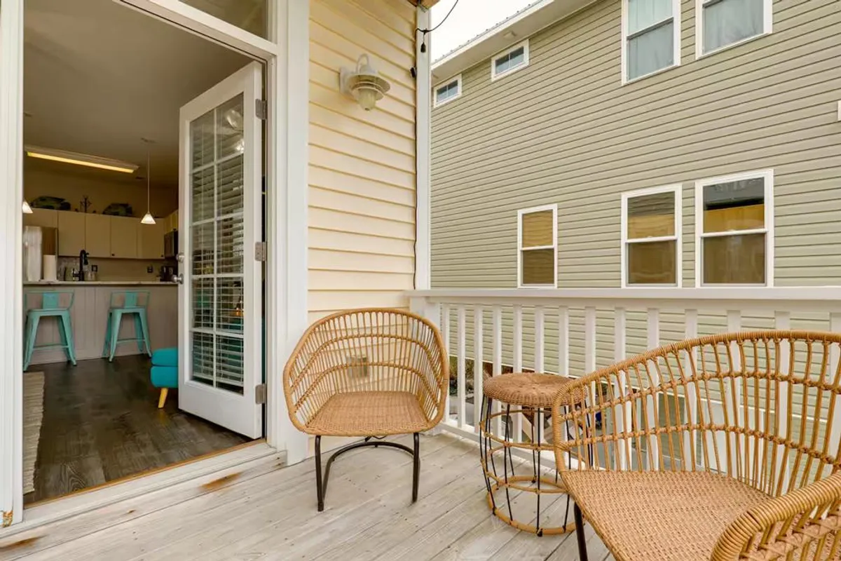 A cozy interior view featuring woven chairs and an open door leading to a visible kitchen area. The arrangement suggests a relaxed transition between indoor and porch spaces, capturing the atmosphere of morning coffees or evening gatherings.